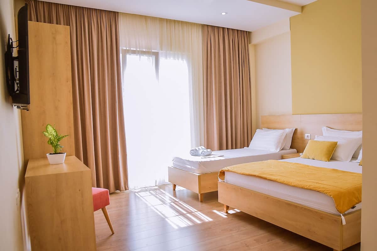 A hotel room with a bed, bedside table, a small desk with a plant, and a TV on the wall.