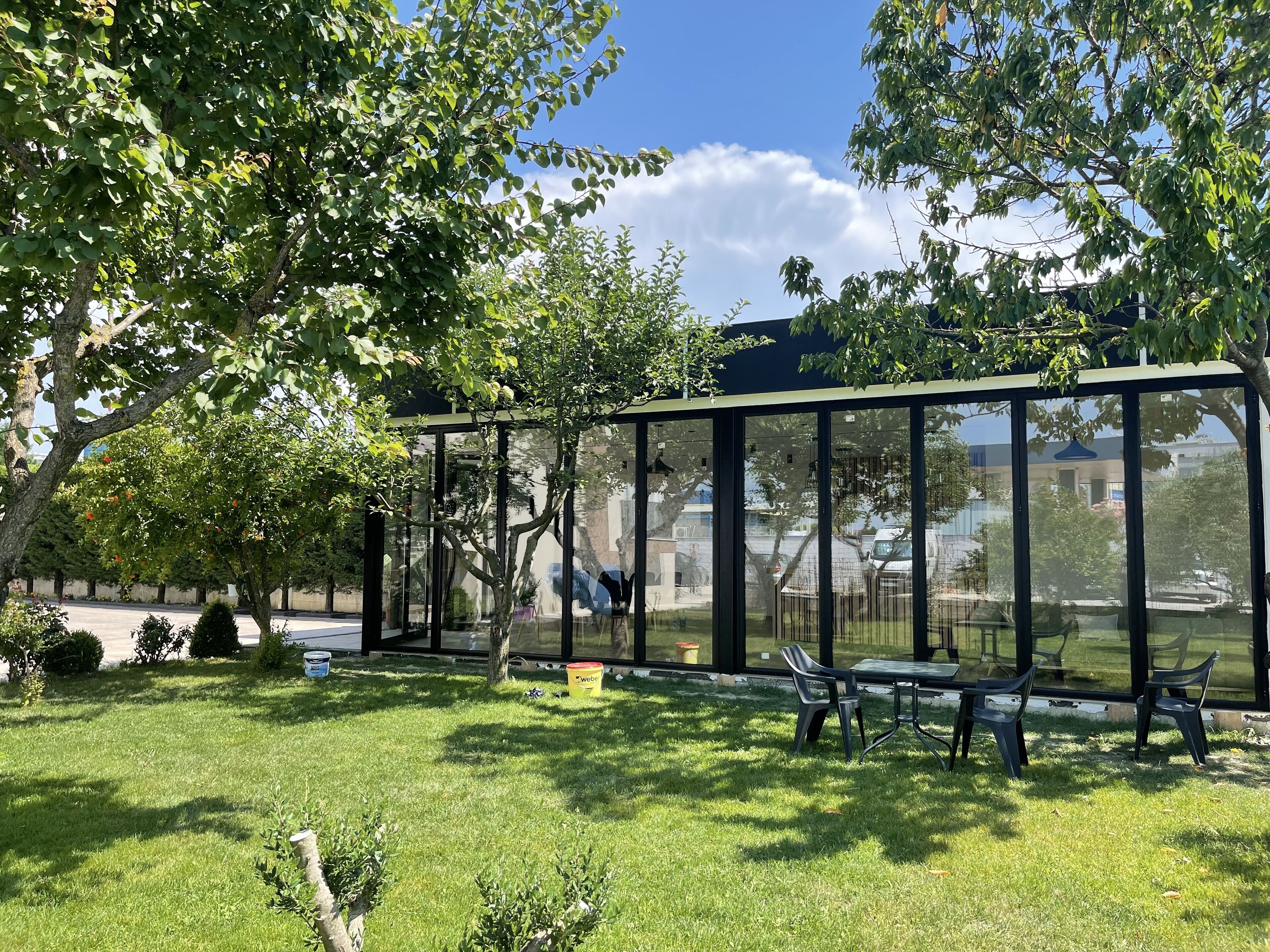 Una estructura moderna de vidrio con asientos, rodeada de abundante vegetación y árboles.