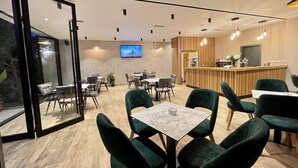 A modern dining area with green upholstered chairs, marble-topped tables, and a wooden reception desk. - Airport Garden Hotel (Nikël)