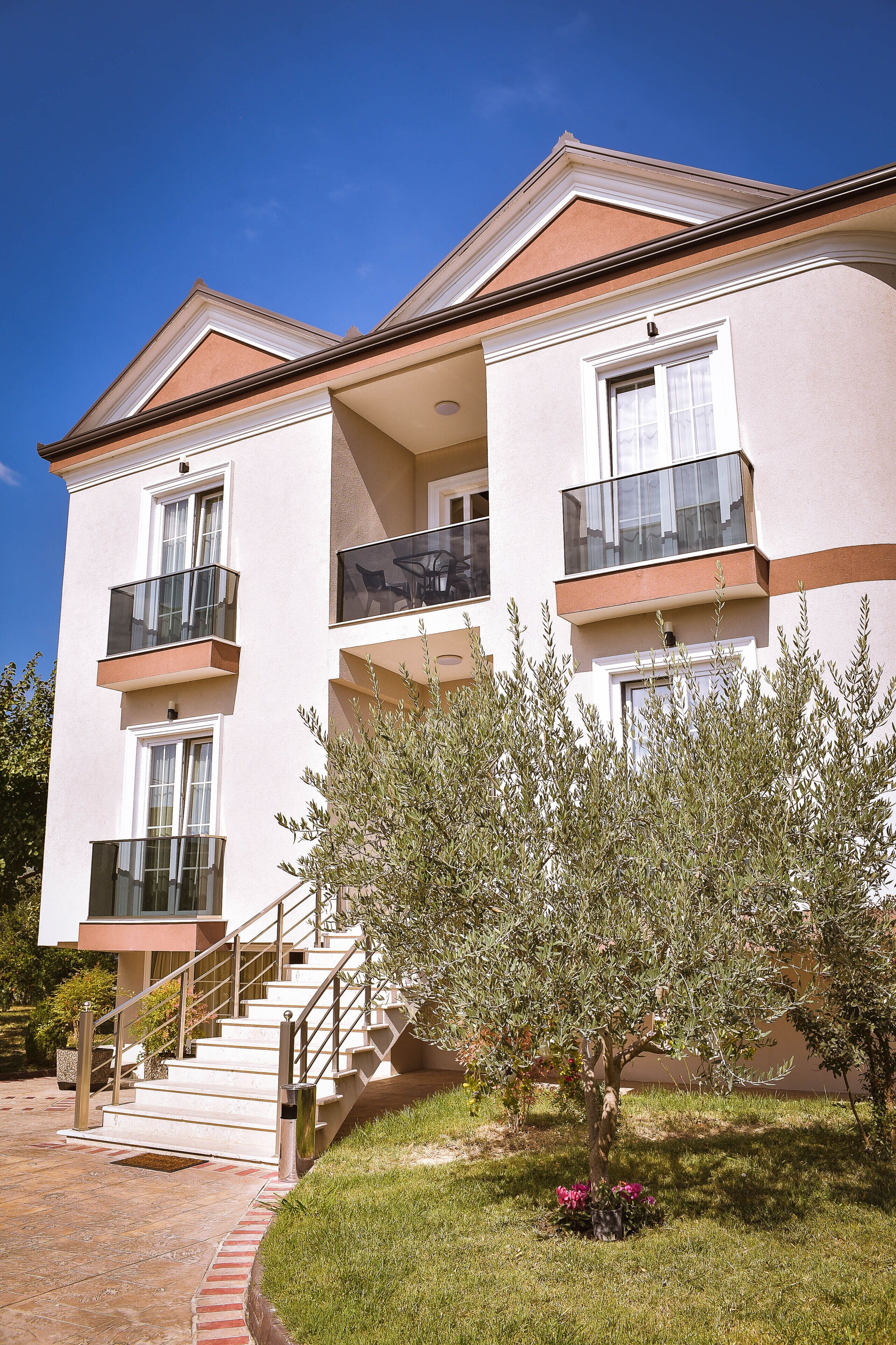 A two-story building with a balcony on the second floor, a staircase leading to the entrance, and a small tree in the front yard.