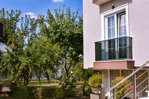Un edificio moderno con balcón de vidrio y jardín con manzanos.