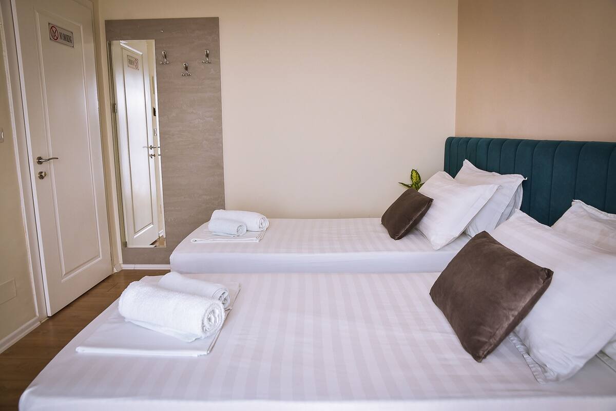 A hotel room with two beds, each with a pillow and a rolled towel.