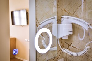 Un baño con un secador de pelo fijado en una pared de mármol, un espejo y un televisor en la pared.