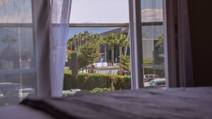 A view from a window with a view of a building, palm trees, and parked cars. - Airport Garden Hotel (Nikël)