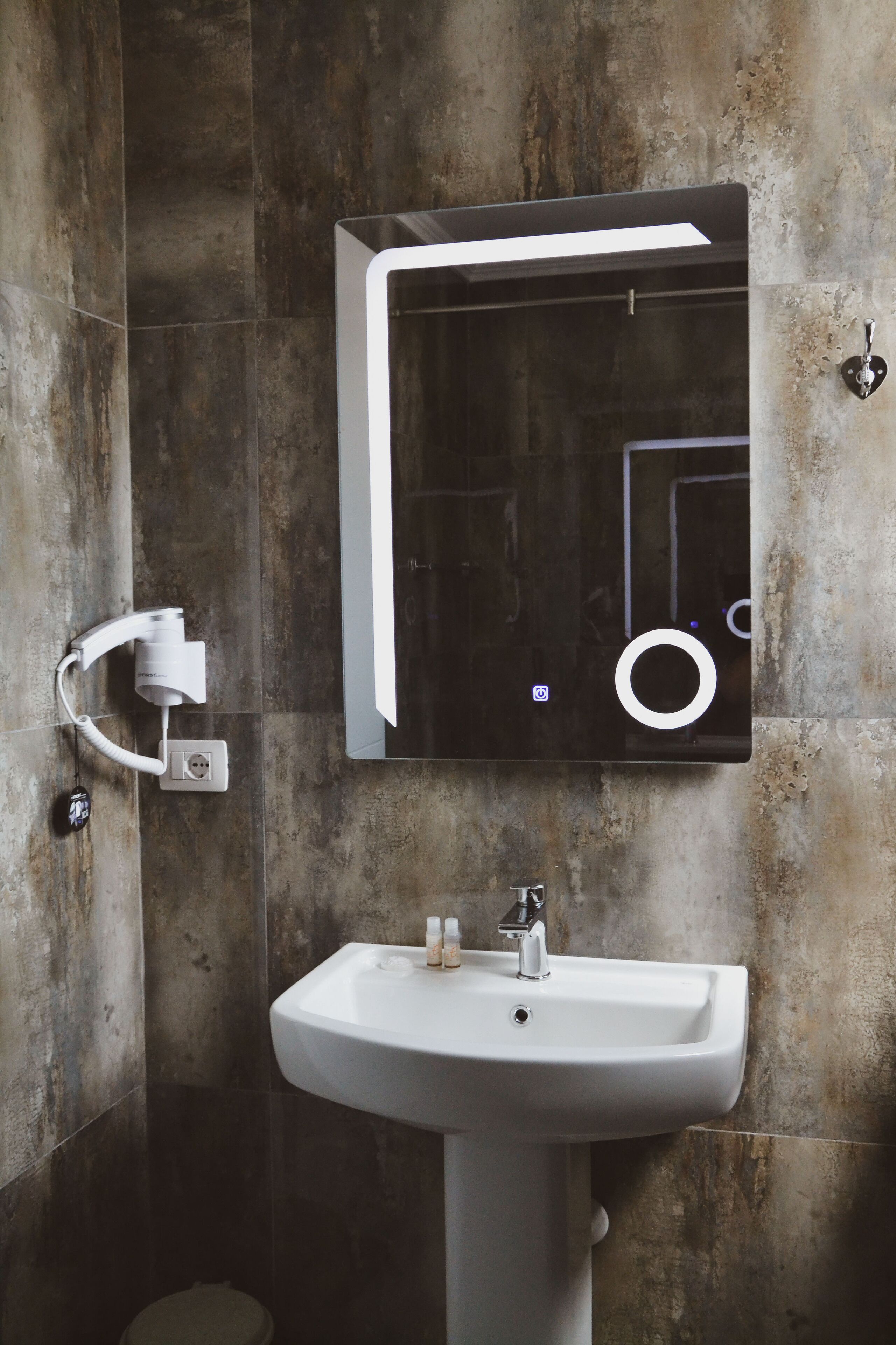 A bathroom with a white sink, a mirror, and a handheld showerhead mounted on the wall.