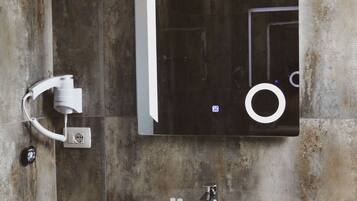 A bathroom with a white sink, a mirror, and a handheld showerhead mounted on the wall.