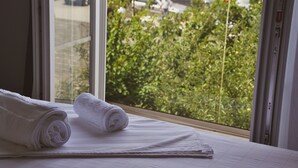 A neatly made bed with rolled white towels, a window with a view of greenery and parked cars outside. - Airport Garden Hotel (Nikël)