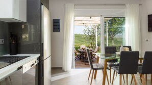 A modern kitchen with a built-in oven and a dining area with a glass table and chairs. - MariAndry Villa, Secluded Retreat with Pool & HotTub (Episkopi, Rethimno)