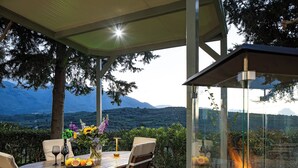 An outdoor dining area with a table set for two, surrounded by chairs, a fire feature, and a view of mountains. - MariAndry Villa, Secluded Retreat with Pool & HotTub (Episkopi, Rethimno)