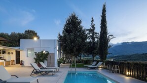 A poolside area with lounge chairs, a small building, and a view of mountains. - MariAndry Villa, Secluded Retreat with Pool & HotTub (Episkopi, Rethimno)