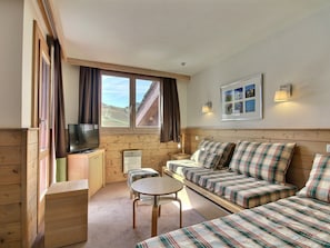 A cozy cabin interior with a sofa, a television, a small table, and a window with curtains.