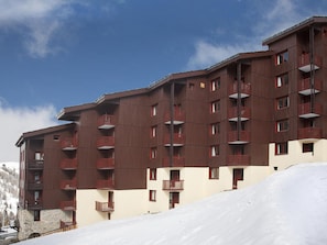 Un hotel de varios pisos con balcones, situado en una zona nevada con cielo despejado.