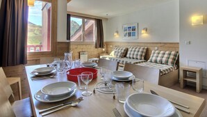 A dining area with a wooden table set for four, a sofa with plaid cushions, and a window with a view of a mountain. - Large duplex for 6/7 near slopes at Belle Plagne (Belle Plagne)