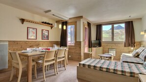 A cozy room with a wooden dining table, chairs, a bed with plaid bedding, a television, and a window with a view of a mountainous landscape. - Large duplex for 6/7 near slopes at Belle Plagne (Belle Plagne)