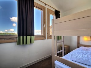 Dormitorio con literas, ventana, cortinas y mesita de noche.