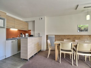 A compact kitchen with a dishwasher, a coffee maker, and a wooden dining table with chairs.