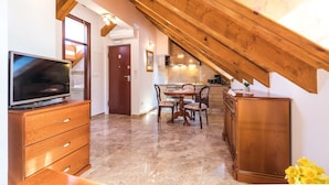 Une pièce spacieuse avec un plafond en bois, un coin repas comprenant une table et des chaises, un téléviseur posé sur un meuble en bois, et une porte donnant sur une autre pièce.