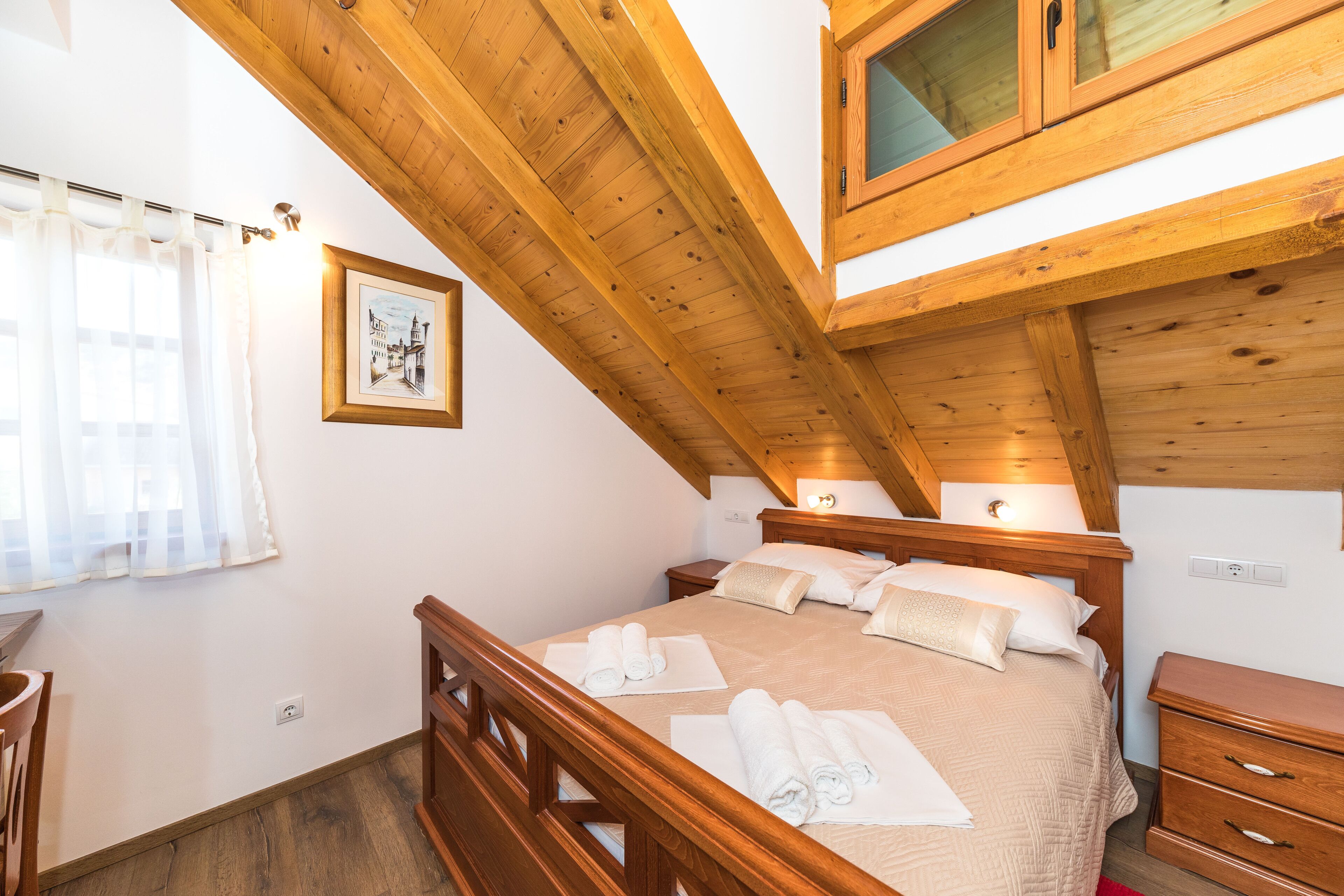Una camera da letto con soffitto in legno, un letto con lenzuola bianche, un comodino e un settimino in legno.
