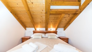 Une chambre avec un plafond en bois, un lit recouvert de draps blancs, deux tables de chevet et une petite table de nuit.