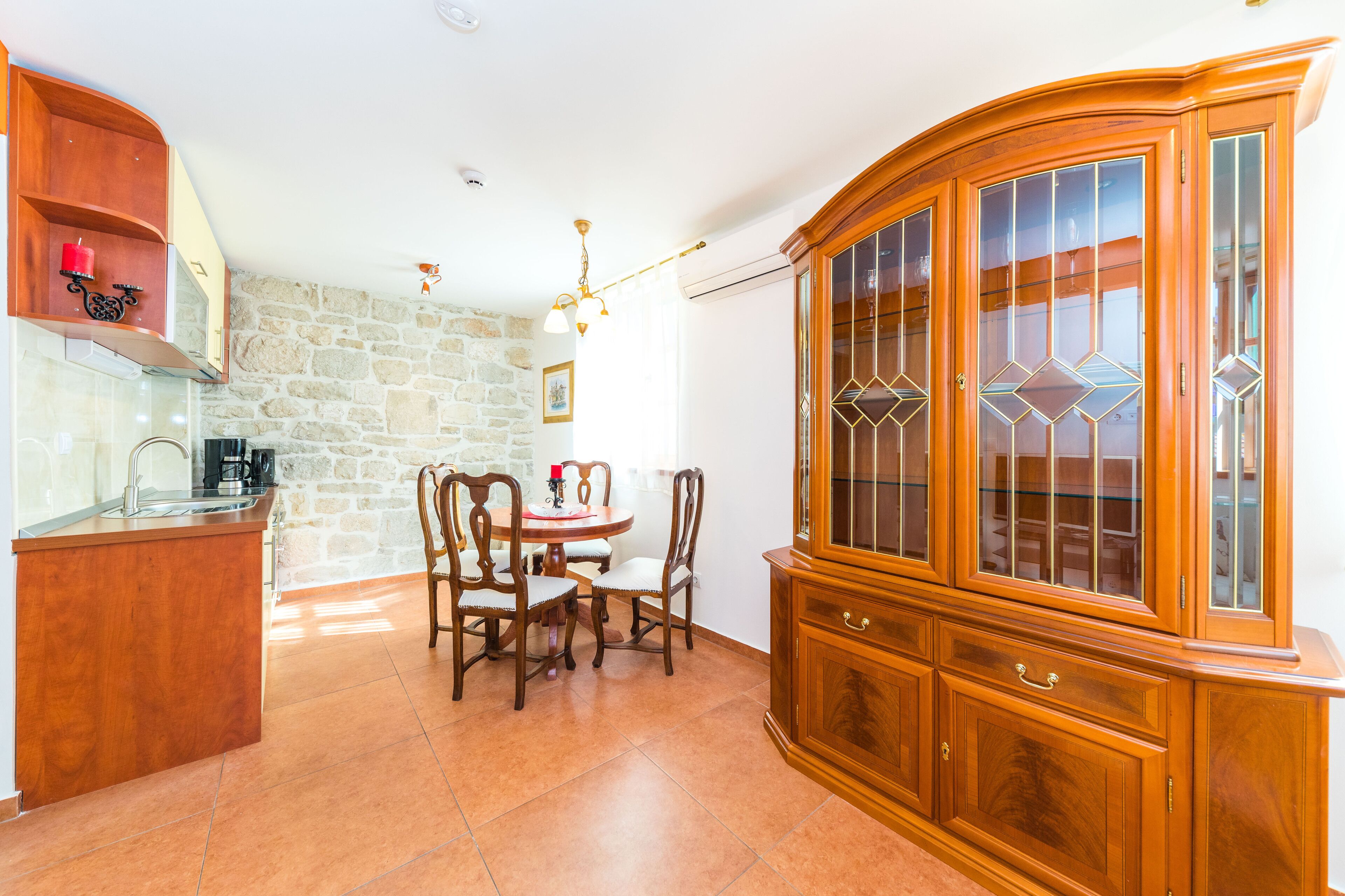 A kitchen with a dining table, chairs, a wooden cabinet, and a stone wall.