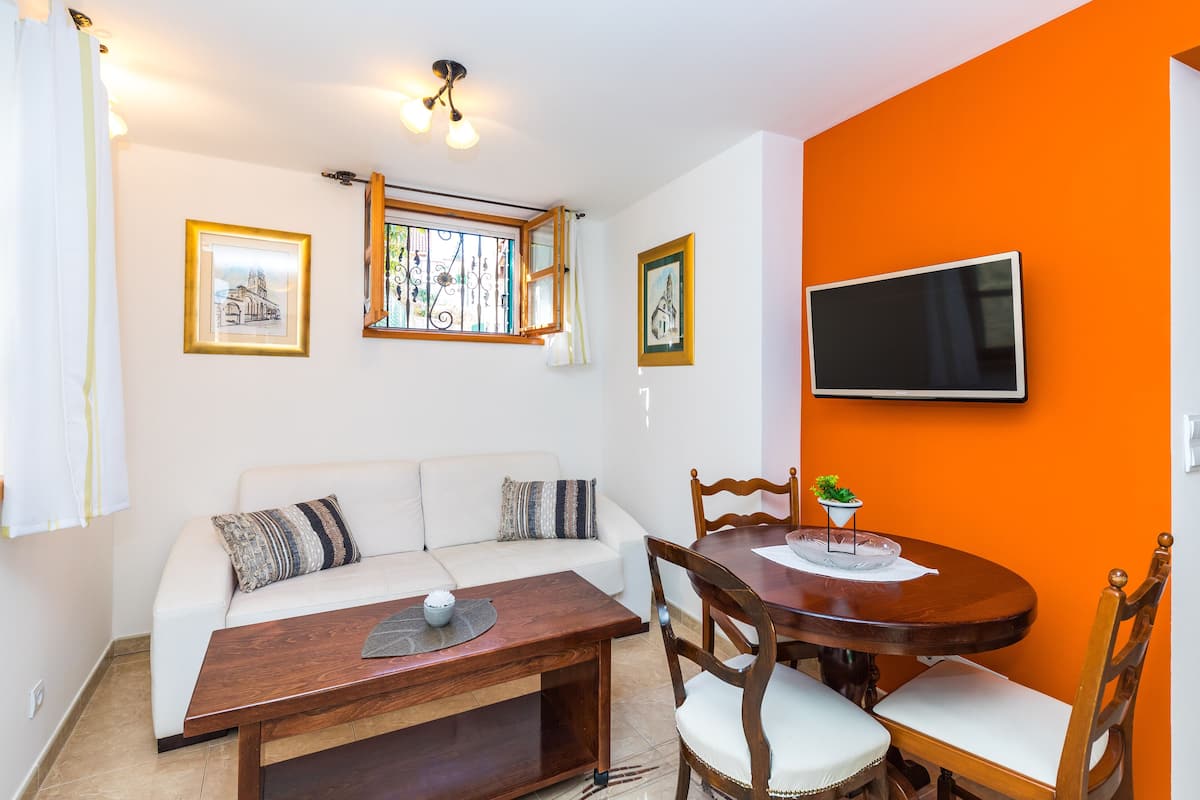 Ein Wohnzimmer mit weißem Sofa, Couchtisch aus Holz und einer orangefarbenen Wand.
