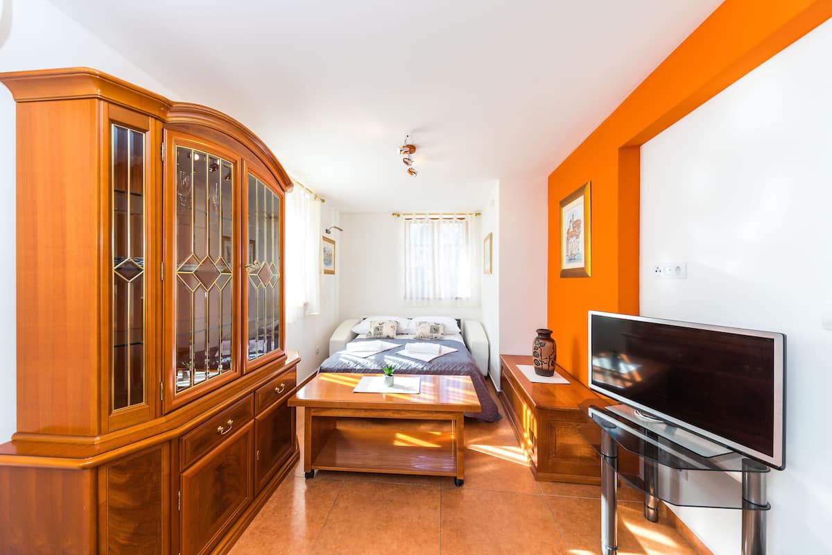 Ein Schlafzimmer mit einem Bett, einem Holzschrank, einem Fernseher auf einem Schrank und einem Fenster mit Vorhängen.