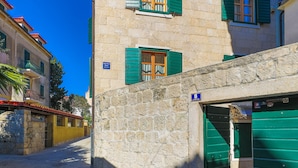 Un bâtiment en pierre avec des volets verts, une porte bien visible et un ciel bleu clair.