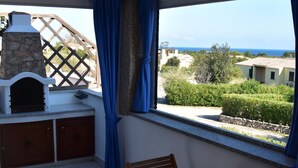 Eine Terrasse mit Holztisch und -stühlen, einem Steinkamin und Blick auf das Meer und die Bebauung.