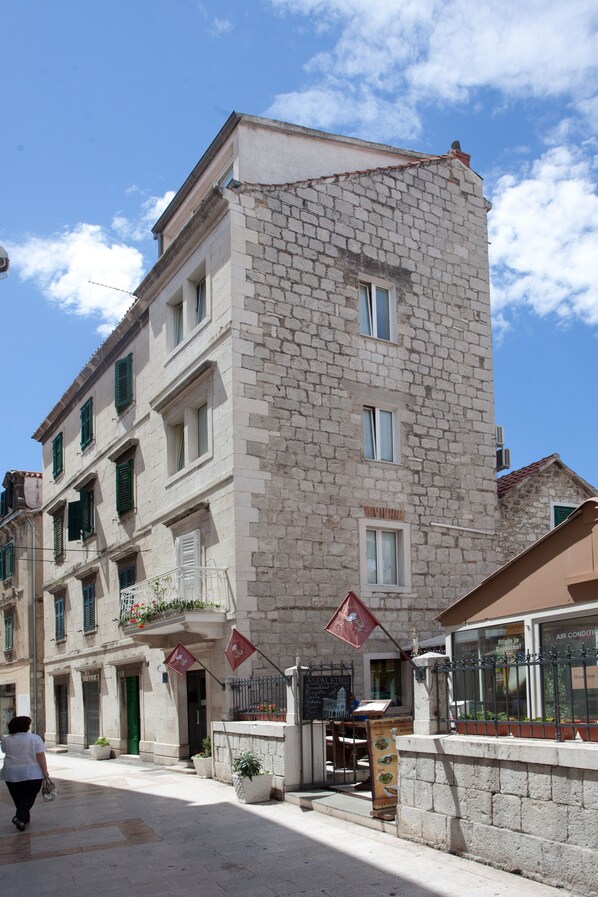 A stone building with multiple windows and balconies, a signboard, and a pedestrian walking by.
