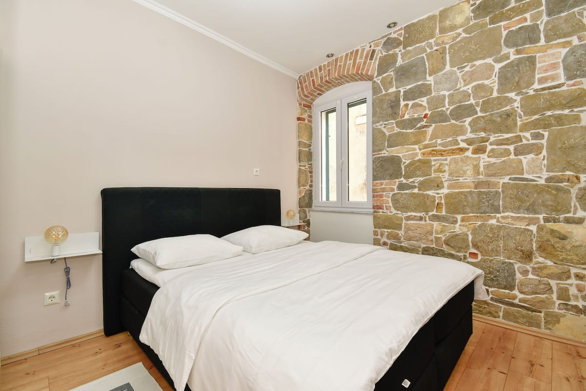 Un dormitorio con pared de piedra, cabecero negro y ventana.