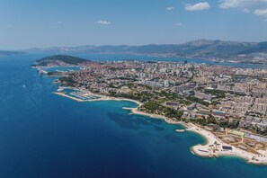 An aerial view of a coastal city with a marina, residential areas, and a mountainous backdrop.
