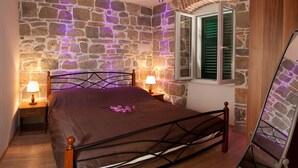 Ein Schlafzimmer mit einer Steinwand, einem Bett mit Metallgestell, zwei Nachttischen mit Lampen und einem Fenster mit Rollläden.