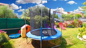 A trampoline with a safety net, surrounded by a garden with various plants and a small playhouse. - Apartment 2042/31807 (Istria - Pula), 5000m from the beach (Pula)