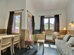 A room with a dining table, chairs, a sofa, a small stool, and a window with curtains. - Duplex for 4, balcony, near slopes (Belle Plagne)