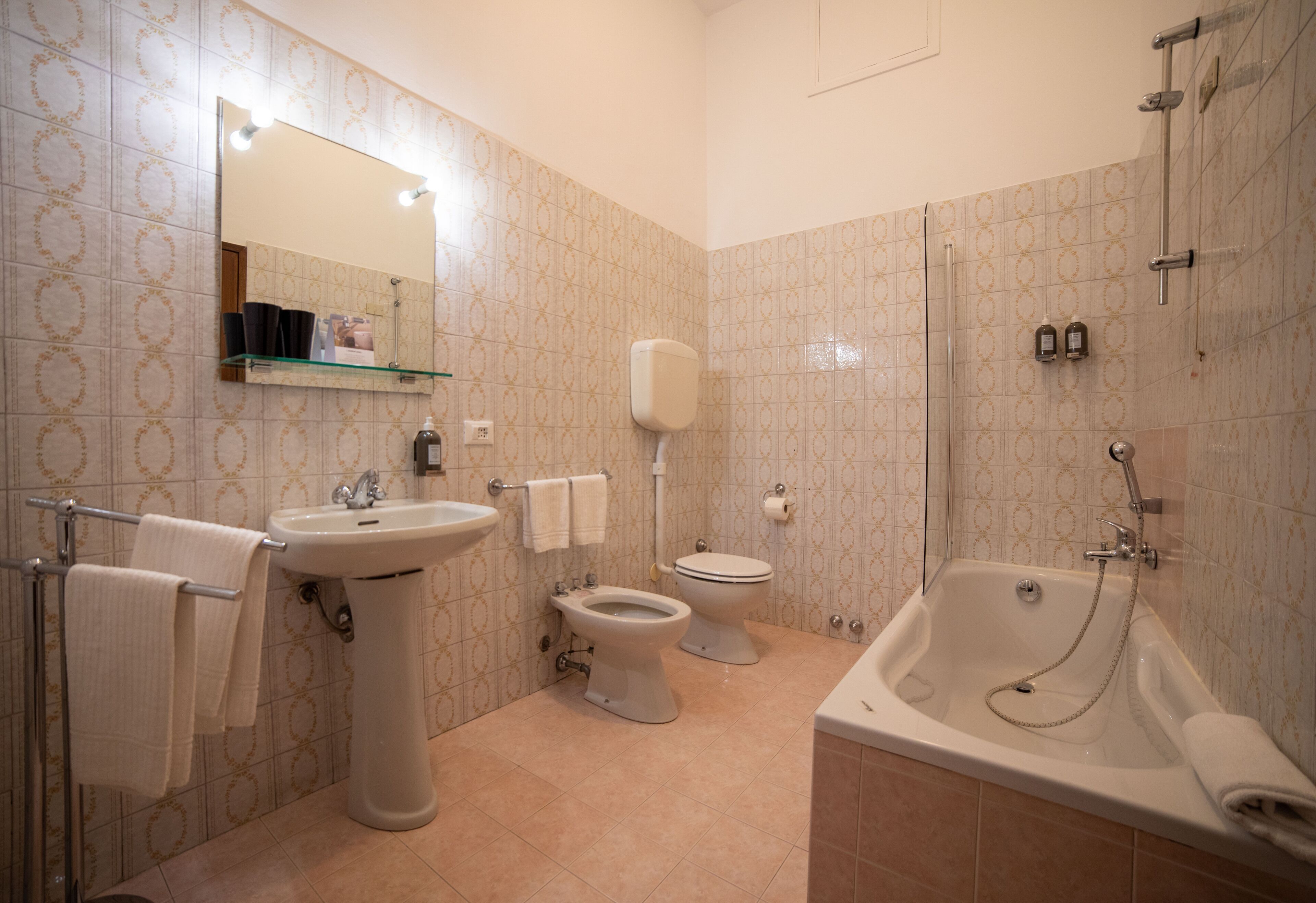 A bathroom with a sink, two toilets, a bathtub, and a mirror with lights.