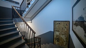 Een trap met een houten leuning en metalen spijlen, die uitkomt op een plateau met een groot kunstwerk met een verweerde uitstraling aan de muur.