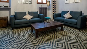 Een woonkamer met twee banken, een salontafel, een vloerkleed met patroon en een kroonluchter.