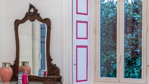 Een kamer met een houten dressoir, een spiegel, een rode stoel en een raam met uitzicht op groen.