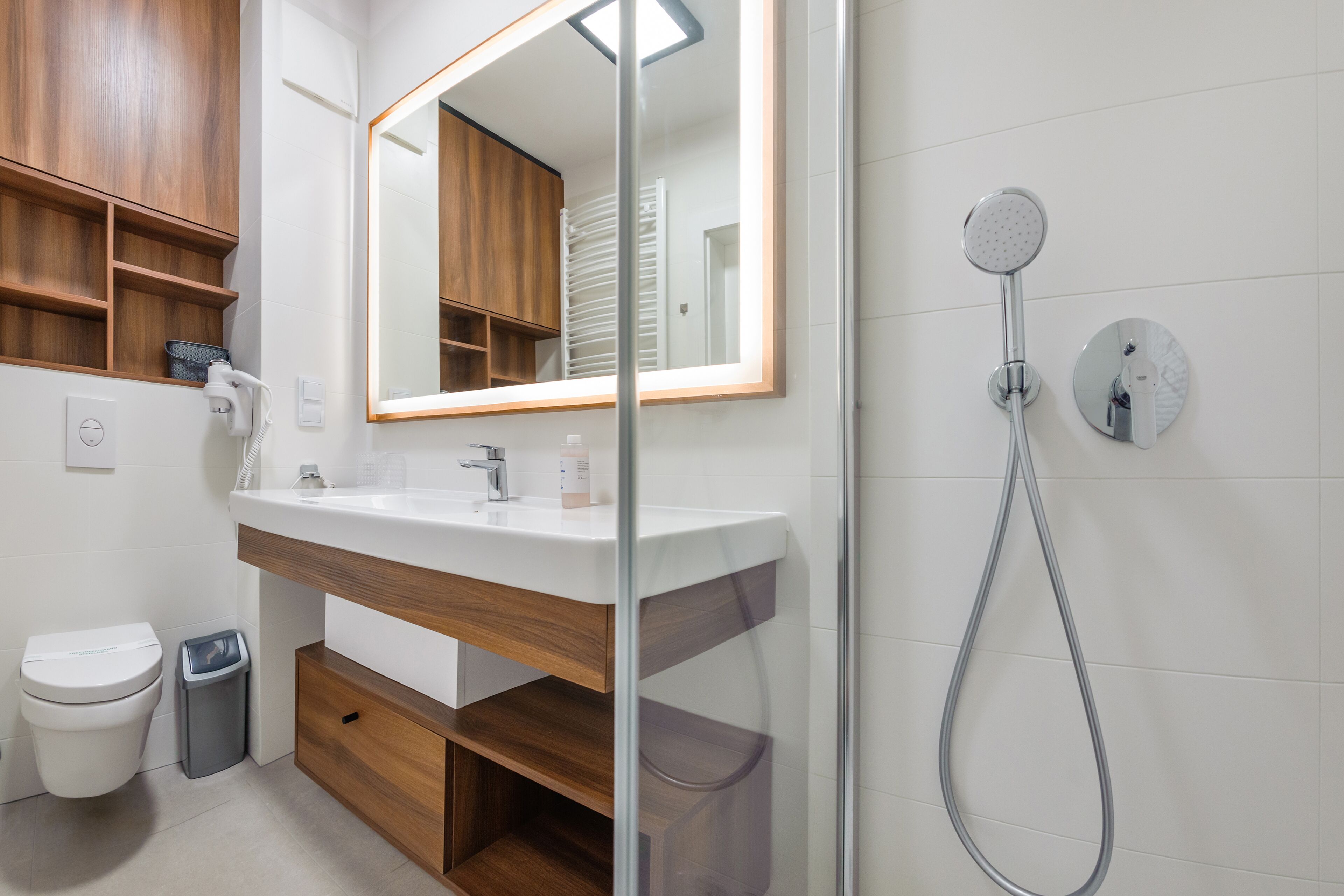 A modern bathroom with a white sink, wooden vanity, a mirror, a shower, and a toilet.