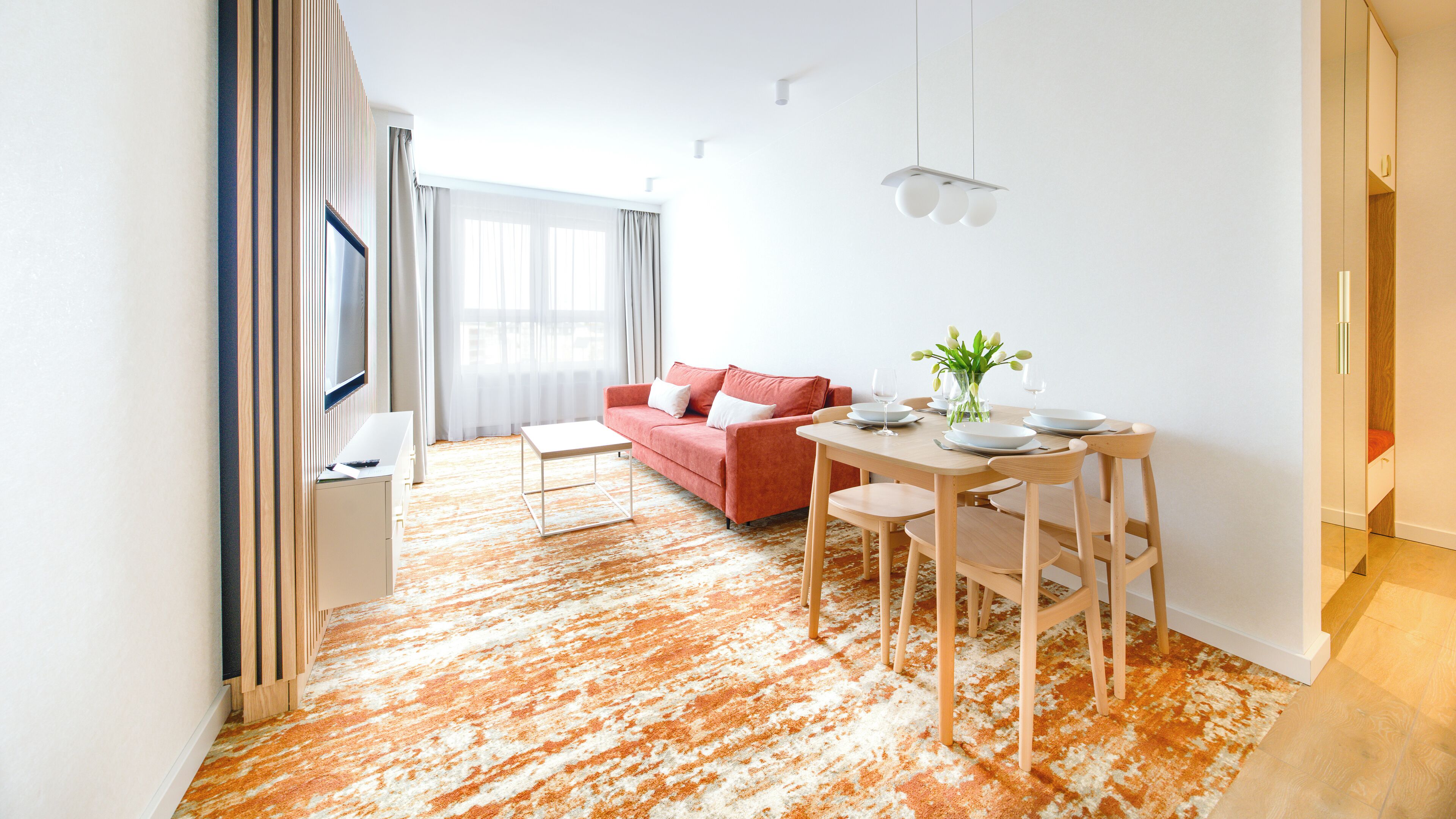 Un salon moderne avec un canapé rouge, une table à manger avec des chaises et une grande fenêtre avec des rideaux.