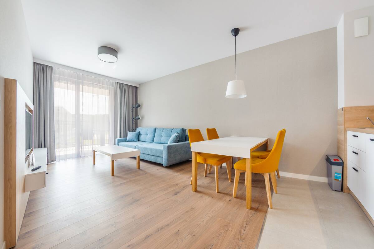 A modern living room with a sofa, dining table, chairs, and a small kitchen area.