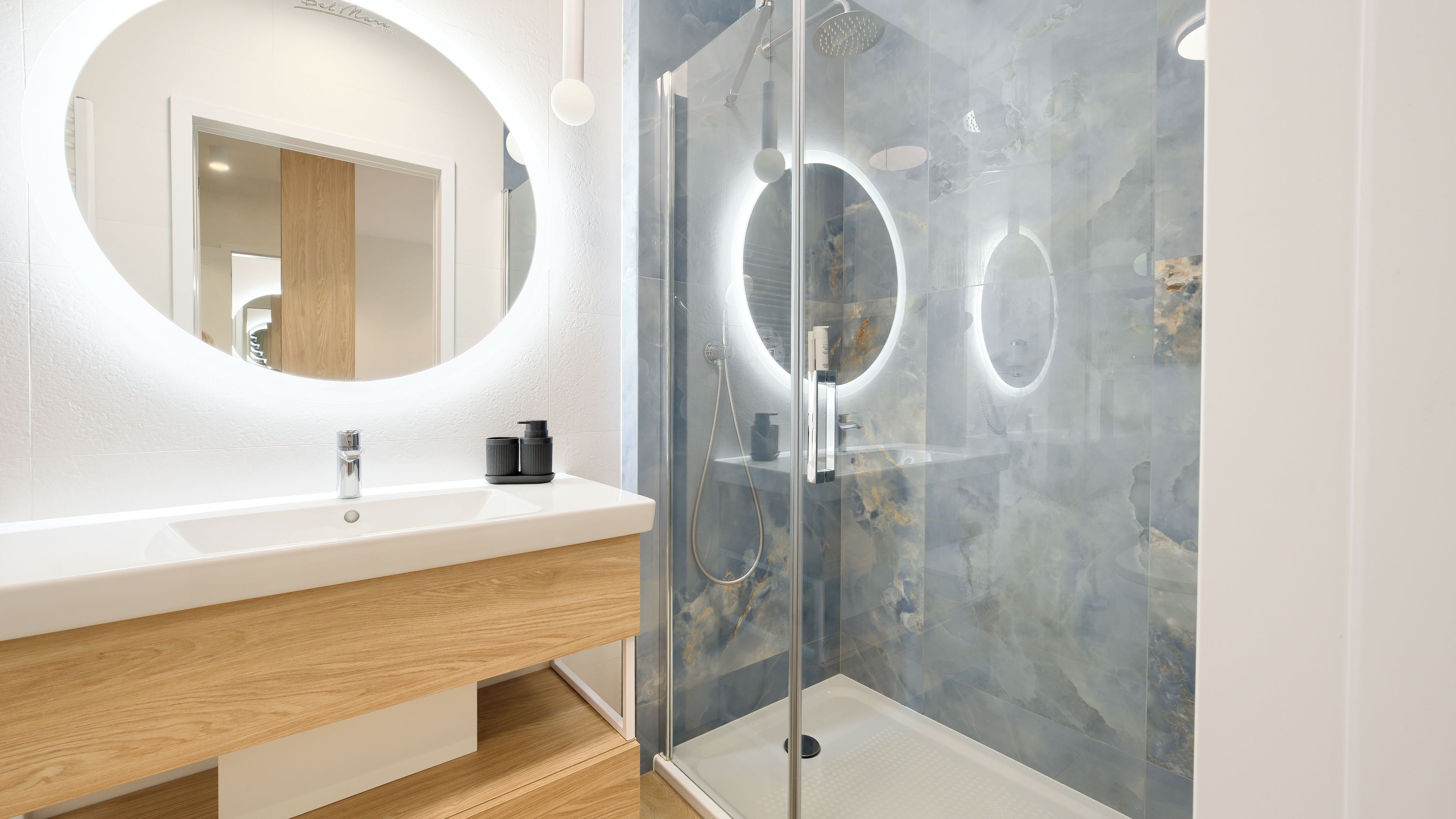 Un baño moderno con ducha envuelta en cristal, un espejo redondo y un lavabo blanco.