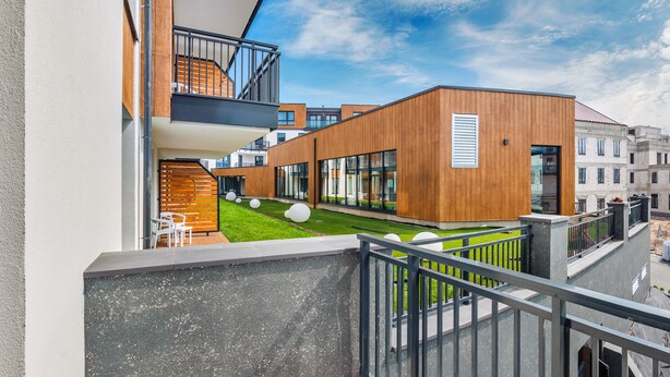 Ein modernes Gebäude mit Holzfassade, einem Balkon mit Metallgeländer und einem grünen Rasen mit kugelförmigen Dekorationen.