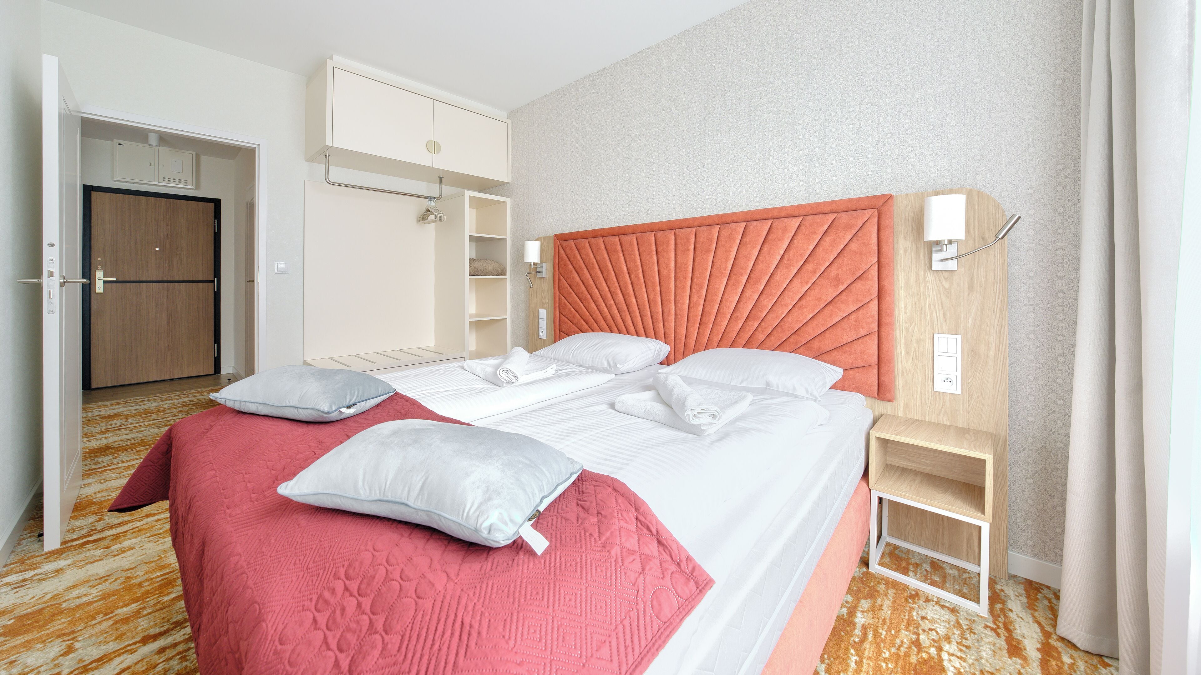 A hotel room with a bed, a wooden wardrobe, a built-in shelf, and a door.