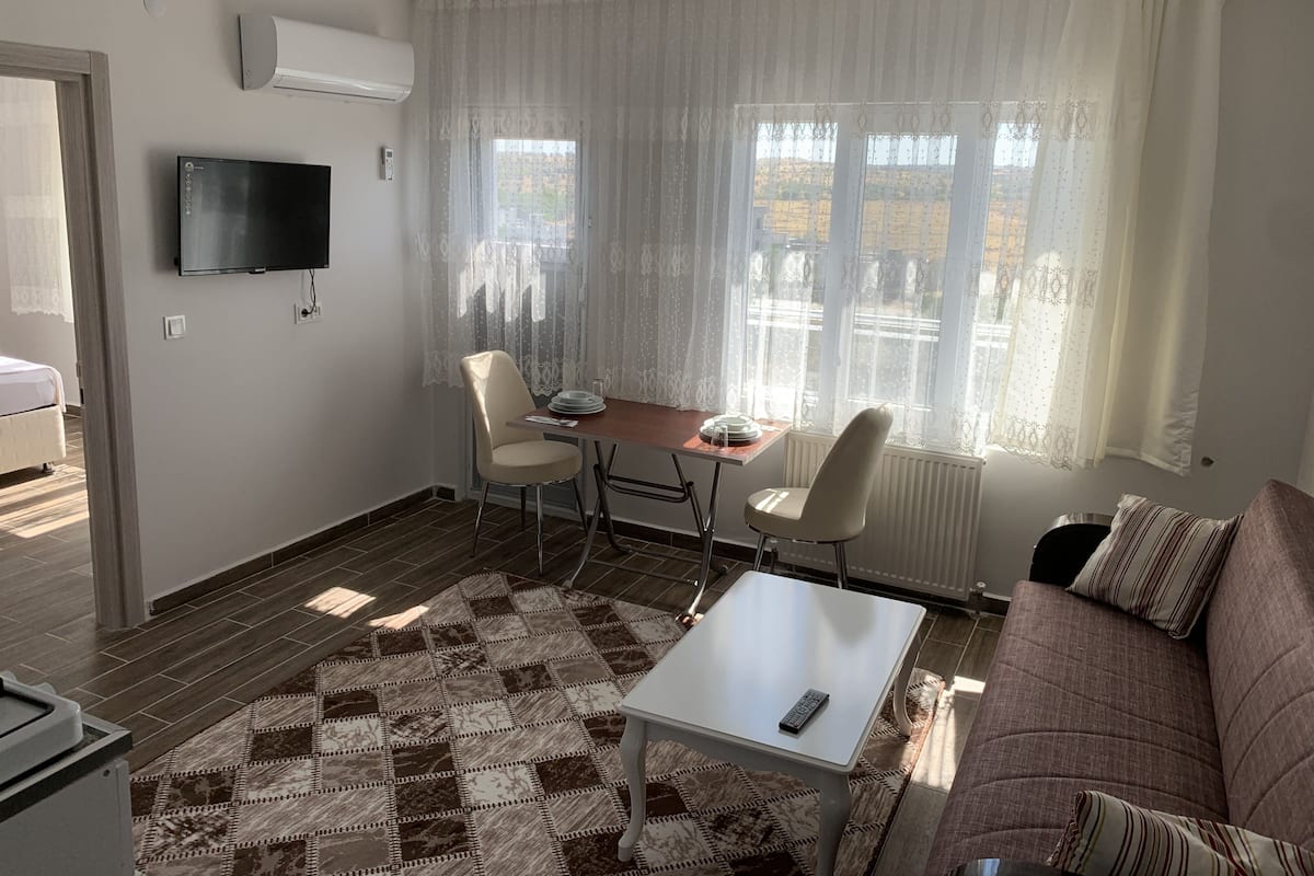 Een woonkamer met een bank, een salontafel, een televisie en een eethoek met stoelen en een tafel.
