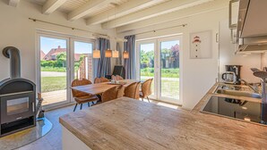 Eine moderne Küche mit einem großen Holztisch, einem eingebauten Herd und Blick auf den Garten durch große Fenster.