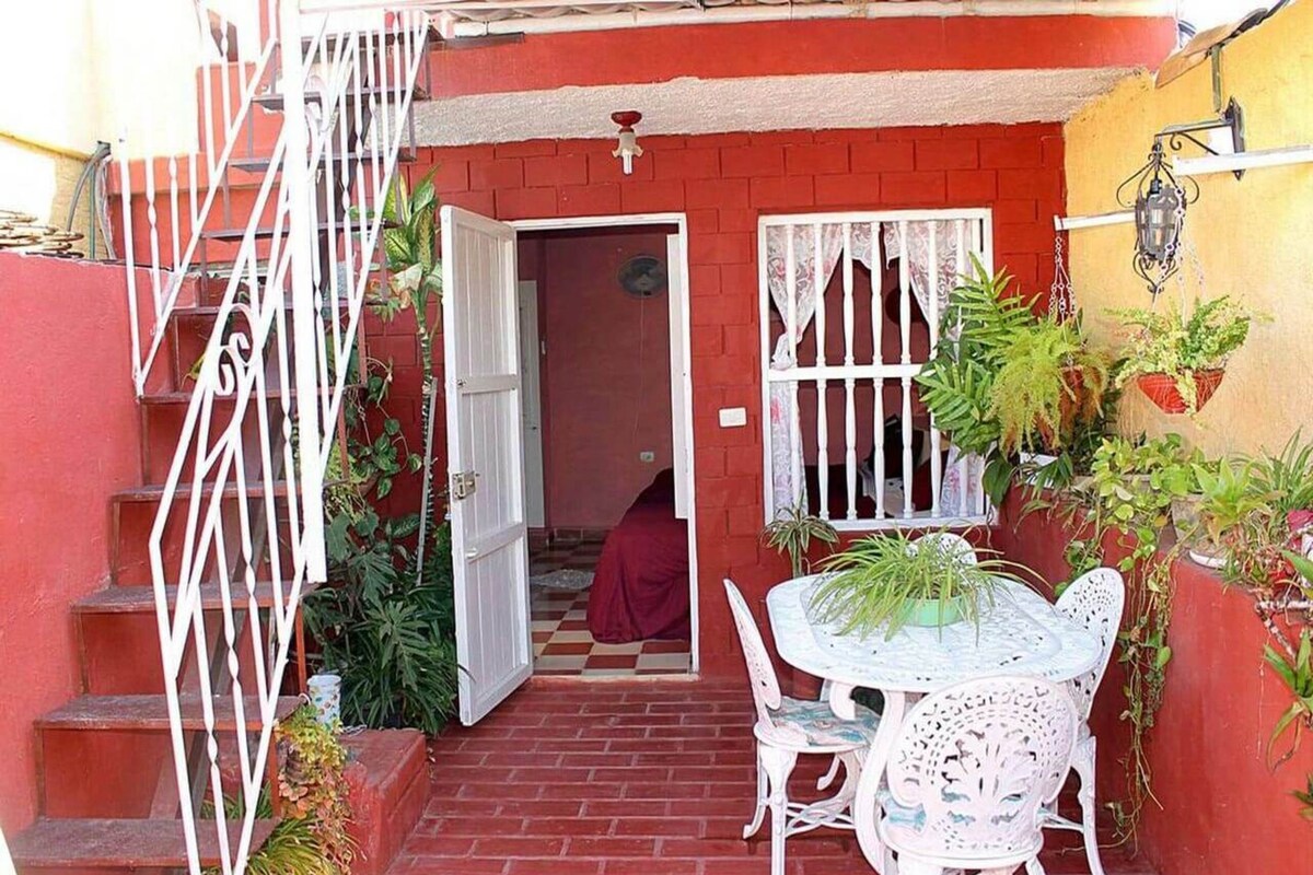 A red brick building with a white gate, a small table with chairs, and potted plants.