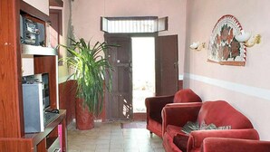 A living room with a red sofa, a wooden entertainment unit, a potted plant, and a door leading outside. - Hostal La Casa Roja TRINIDAD (Trinidad)