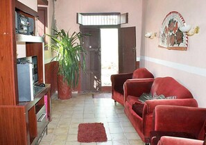 A living room with a red sofa, a wooden entertainment unit, a potted plant, and a door leading outside. - Hostal La Casa Roja TRINIDAD (Trinidad)