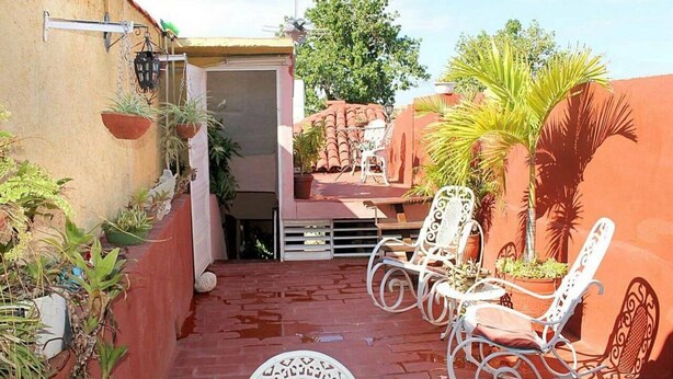 A patio with white rocking chairs and a table, surrounded by potted plants and a small barbecue area. - Hostal La Casa Roja TRINIDAD (Trinidad)